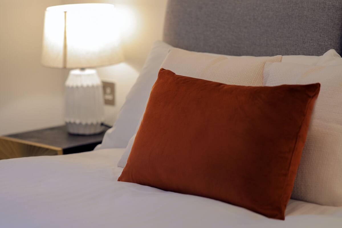 A neatly made bed with white linens and a single brown pillow.