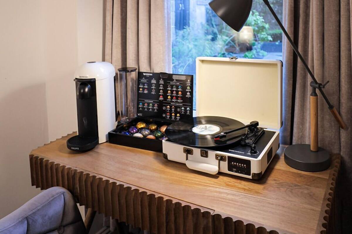 A desk with a turntable, a coffee machine, and a lamp near a window with curtains.