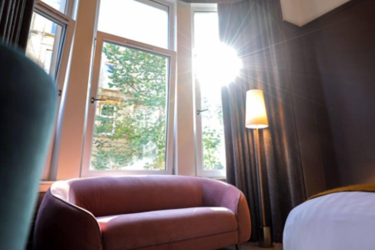A hotel room with a large window, a sofa, a lamp, and a bed.