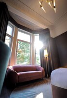 Una habitación de hotel con un ventanal grande, un sofá, una lámpara y una cama.