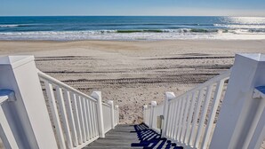 Un escalier en bois menant à une plage, avec des rampes blanches.