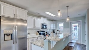 Una cocina moderna con armarios blancos, electrodomésticos de acero inoxidable, encimera de granito y un banco de madera.