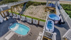 Zona de piscina con jacuzzi, sillas de descanso y una terraza con vista a la playa.