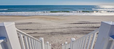 A wooden staircase leading to a beach with white railings.