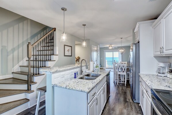 A modern kitchen with granite countertops, stainless steel appliances, and a central island. - Revive! Oceanfront Home | Pool | Hot Tub | Elevator (North Topsail Beach)