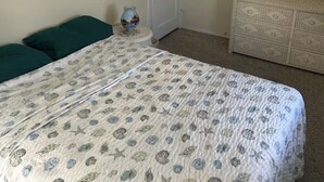 A bedroom with a bed, two green pillows, a dresser, a lamp, and a vase on a small table.