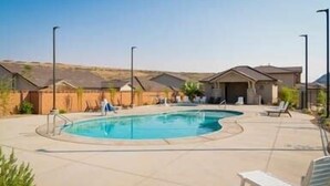 A swimming pool with lounge chairs and a covered area, surrounded by houses.
