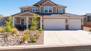 A two-story house with a garage, a landscaped front yard with rocks and small trees, and a clear blue sky.