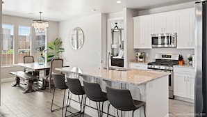 A modern kitchen with white cabinets, a granite countertop, a stainless steel refrigerator, and a built-in oven.