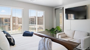 A modern living room with a large bed, a sofa, a coffee table, and a TV mounted on the wall.