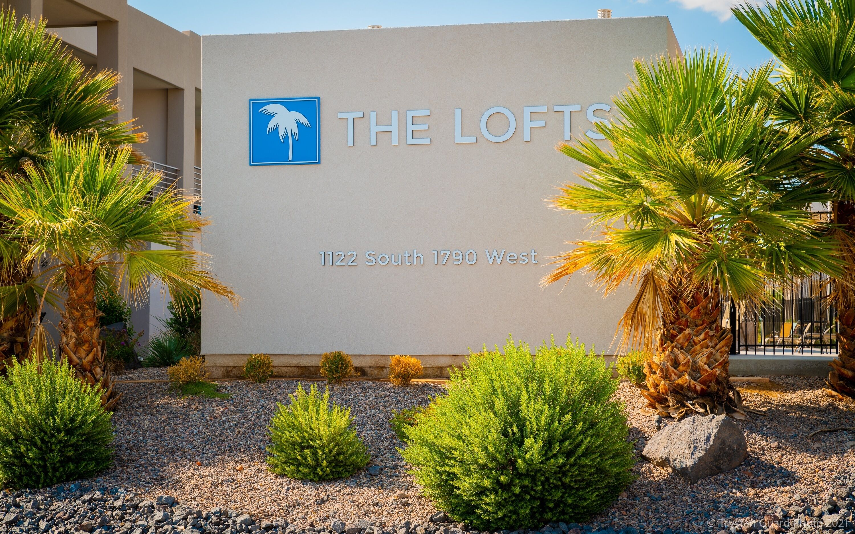 Une enseigne pour le complexe d’appartements « The Lofts », situé au 1122 South 1790 West, avec des palmiers et la façade moderne du bâtiment.