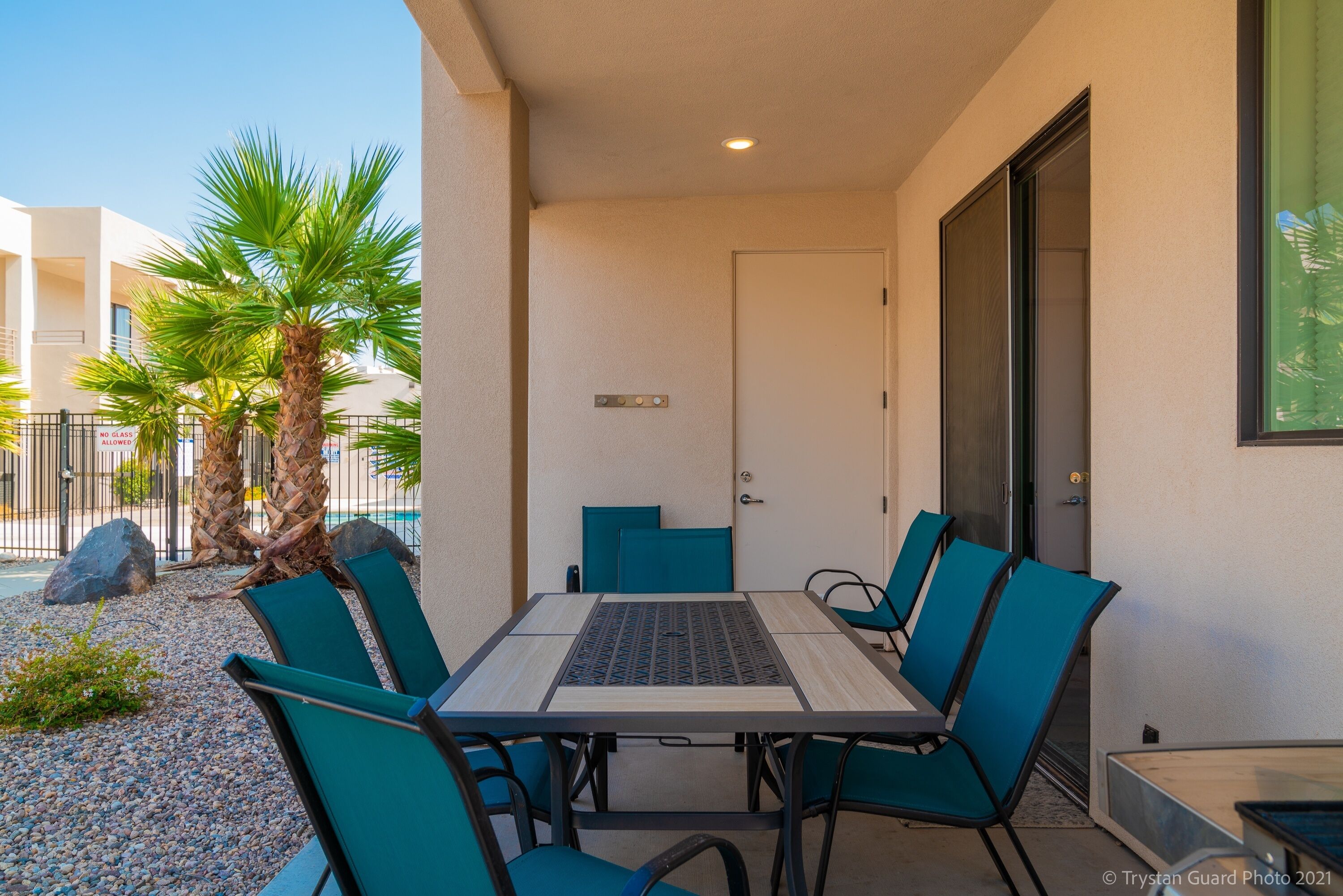 Un patio al aire libre con mesa y sillas, palmeras y un edificio en el fondo.