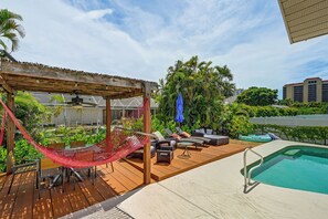 Un espace aménagé au bord de la piscine, avec une terrasse en bois, un hamac, du mobilier d’extérieur et une piscine.