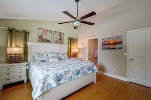 Une chambre à coucher avec un lit, des tables de chevet, un ventilateur de plafond, un tableau et une porte.