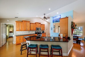 Una cocina moderna con armarios de madera, una isla central con taburetes de bar, un ventilador de techo y un amplio ventanal.