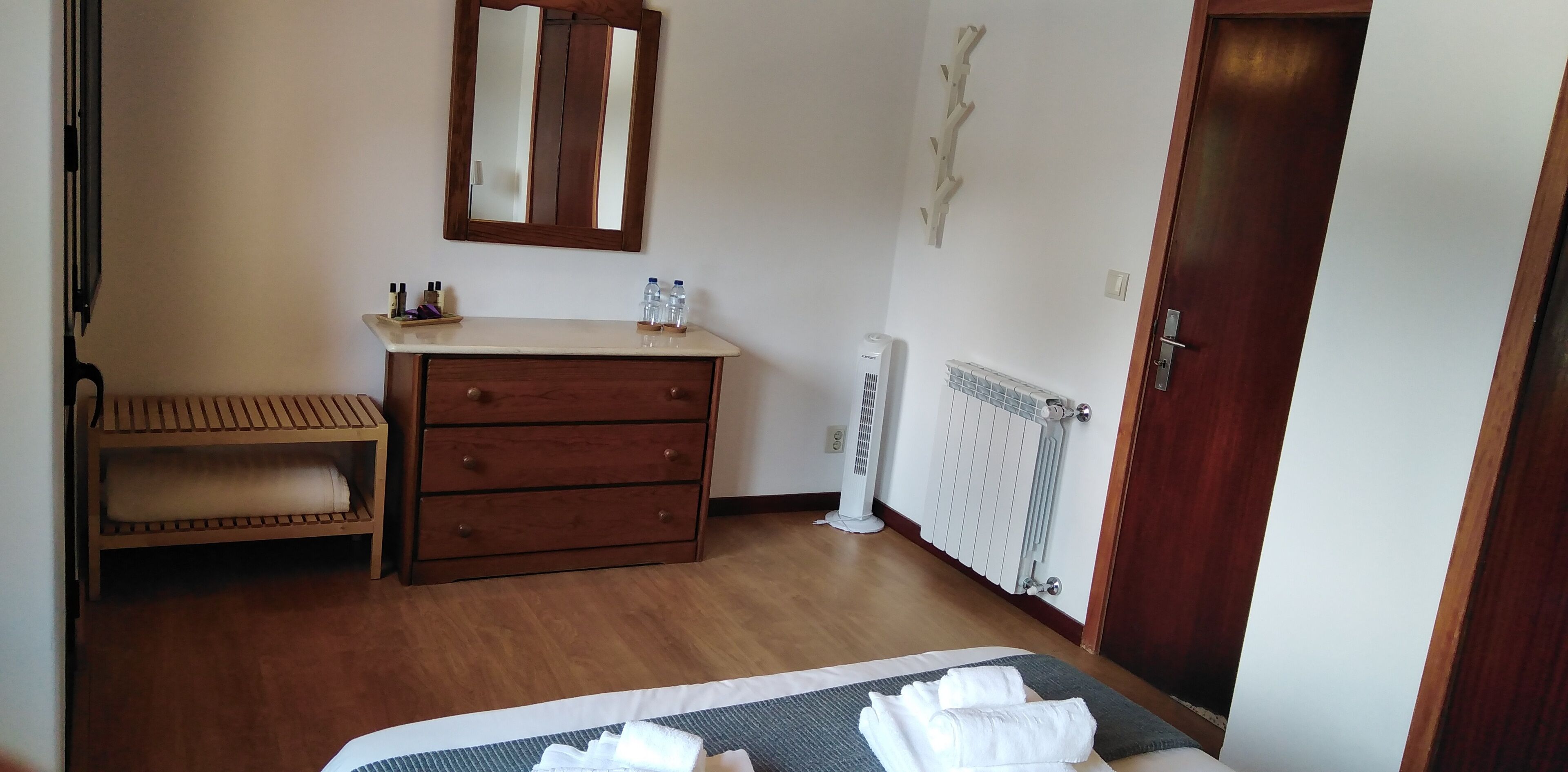 A bedroom with a bed, a wooden dresser, a mirror, a radiator, and a door.