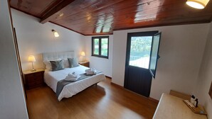 Quarto com cama, duas luminárias de cabeceira, janela e porta.