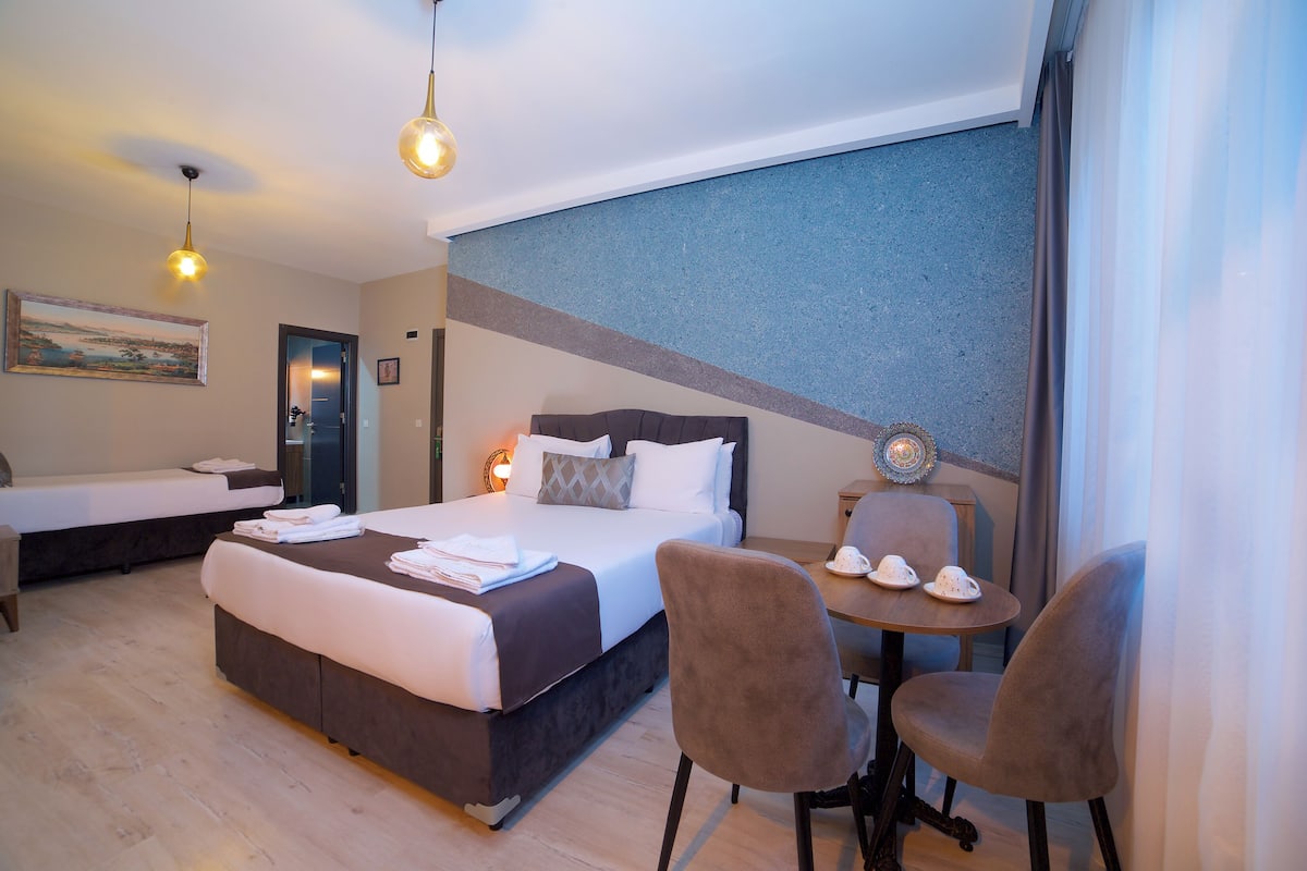 A hotel room with a large bed, two chairs, a small table, and a painting on the wall.