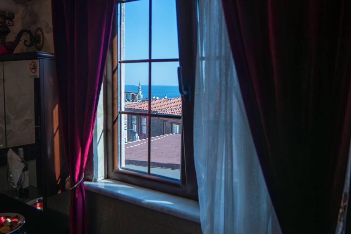 A room with a window, curtains, a chair, and a view of buildings.