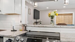 Una cocina moderna con estufa de acero inoxidable, muebles blancos y televisión empotrada.