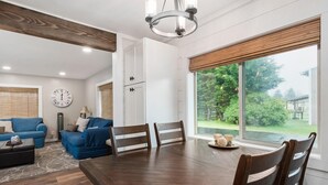 Un salón amplio con una gran mesa de comedor de madera, sofás azules y vistas a un jardín a través de grandes ventanales.