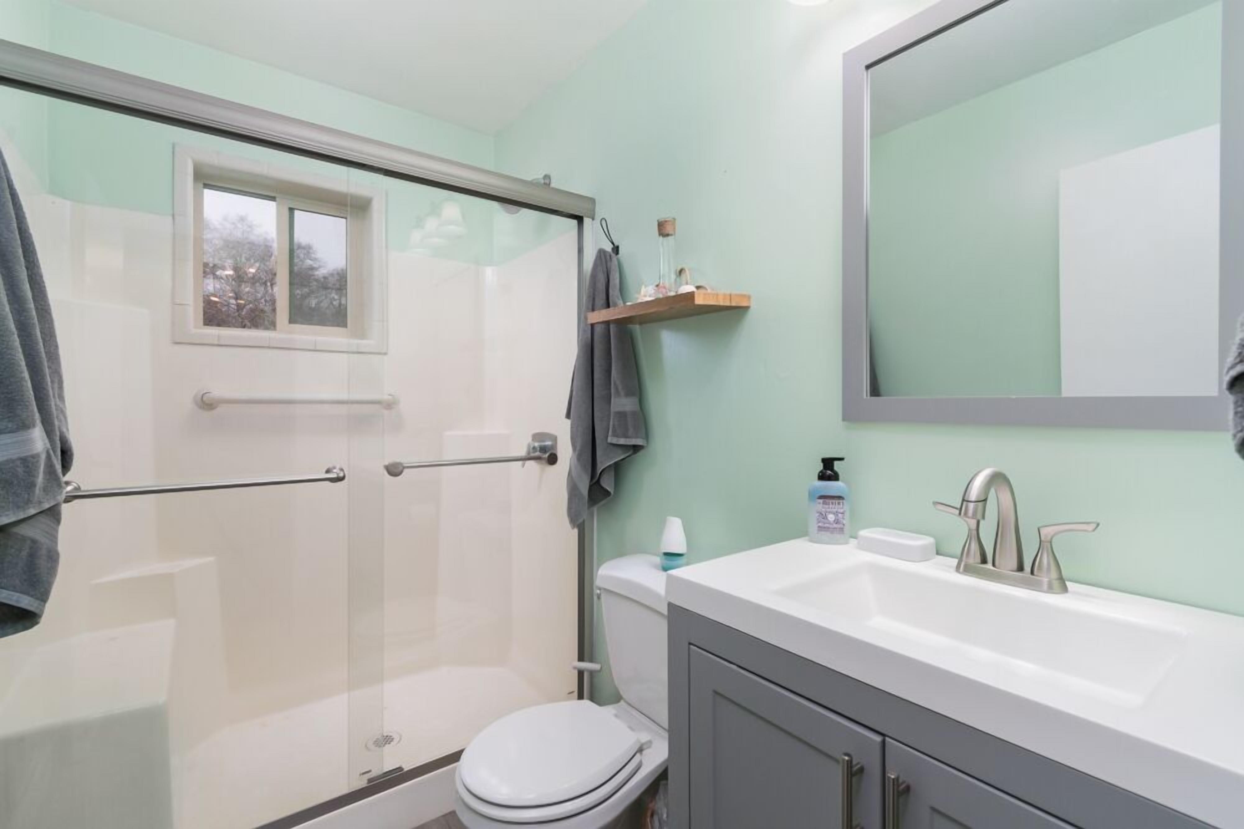 A bathroom with a glass-enclosed shower, a white toilet, a sink with a modern faucet, and a mirror above the sink.