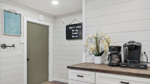 Una cocina con armarios blancos, encimera de madera, cafetera y un letrero en la pared.