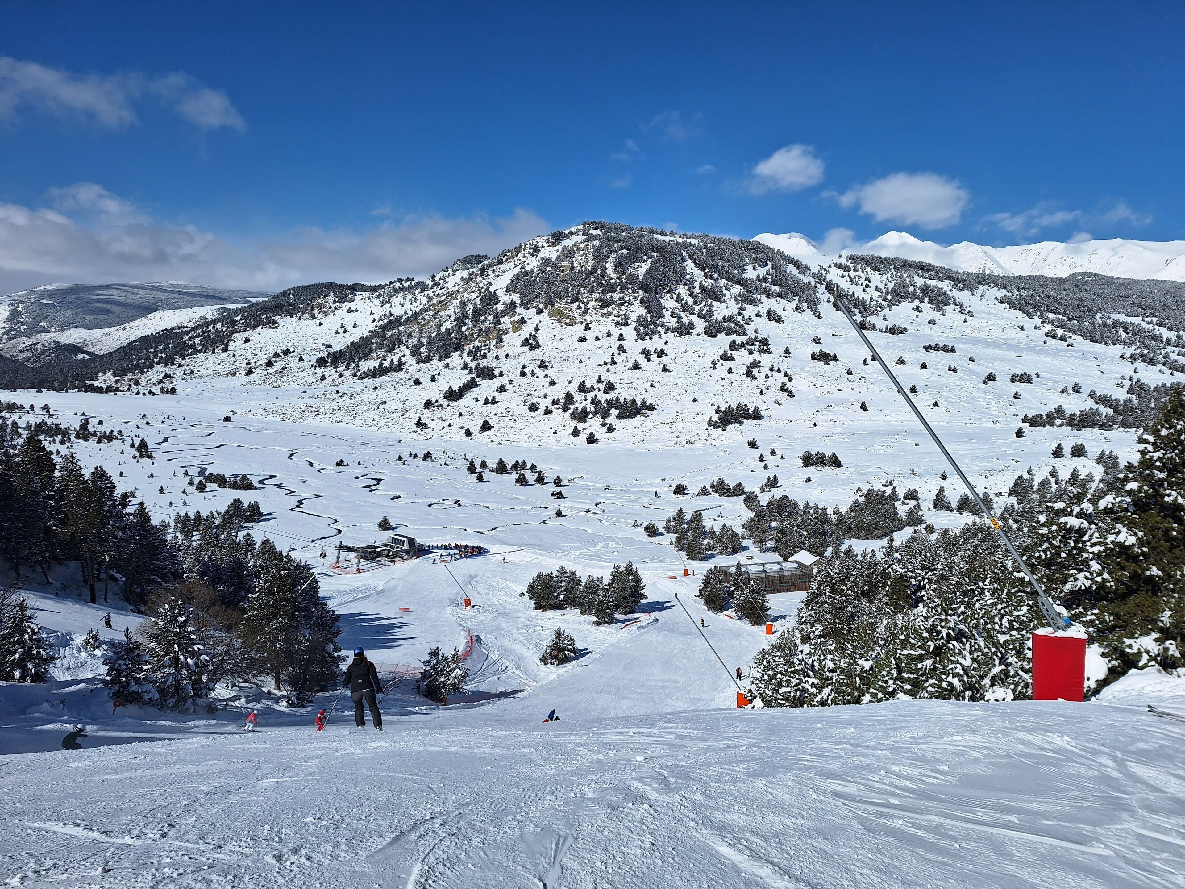 A snowy mountain landscape with a ski slope, trees, and a red building.