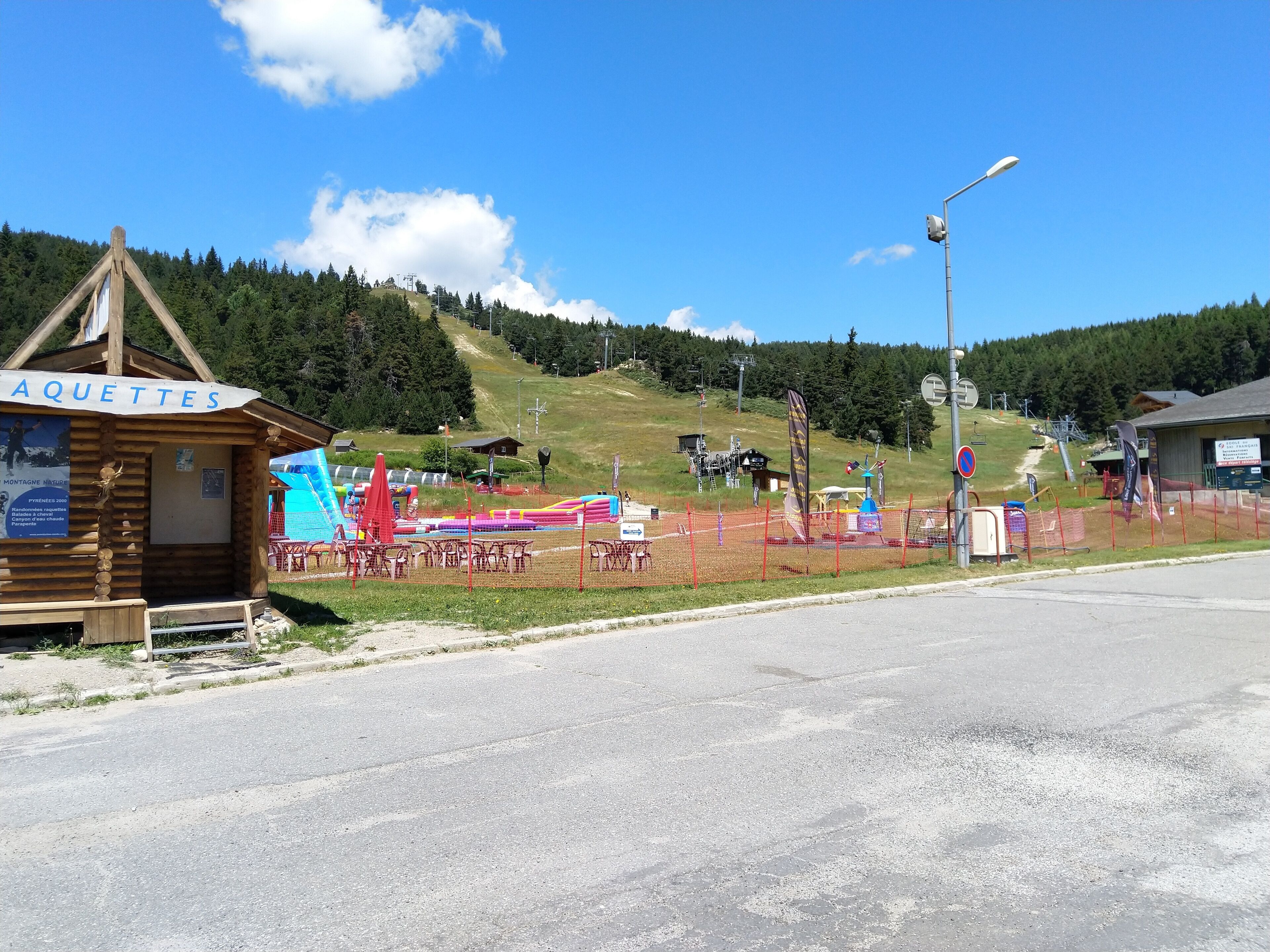 A wooden cabin labeled "AQUETTES" with a signboard, surrounded by a fenced area with inflatable slides and a ski lift in the background.