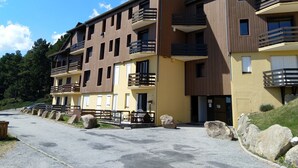 A multi-story residential building with balconies, a paved driveway, and large rocks lining the entrance.