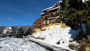 A multi-story building with balconies, surrounded by snow-covered trees and a clear blue sky.