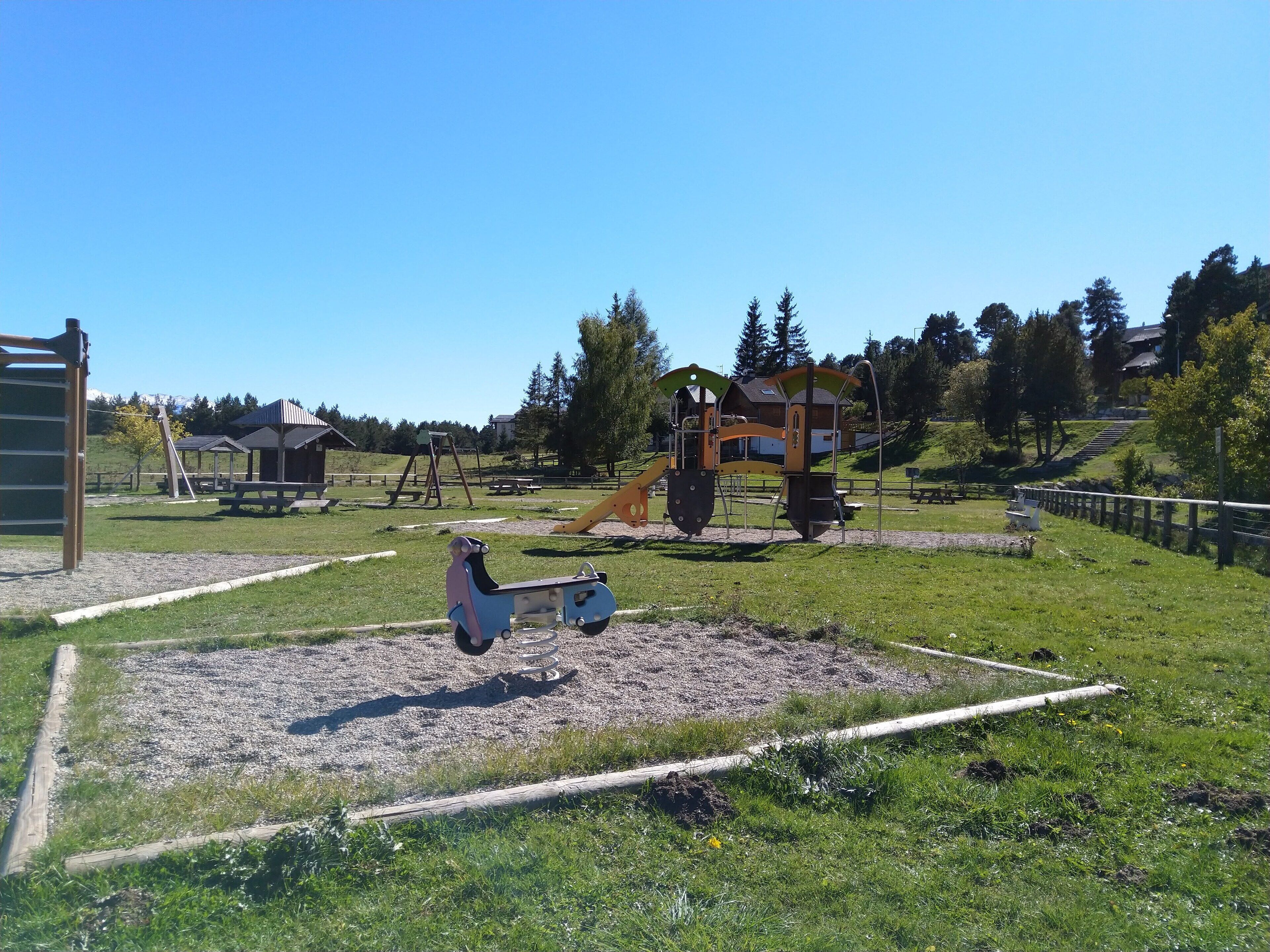 Un parque infantil con diversas estructuras de juego, un espacio para picnic y una zona vallada.