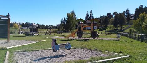 Un parque infantil con diversas estructuras de juego, un espacio para picnic y una zona vallada.