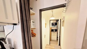 A narrow hallway with a wooden floor, a white door leading to a kitchen area, and a ceiling fan.