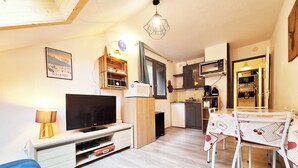 A compact living space with a TV, dining table, and kitchenette.