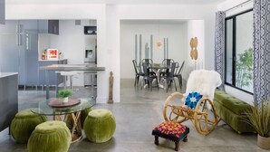 Una sala de estar moderna con una mesa de centro de vidrio, otomanas verdes, un sillón de mimbre y un sofá verde.