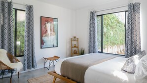 Un dormitorio moderno con una cama grande, una silla, una mesita y una ventana con cortinas estampadas.