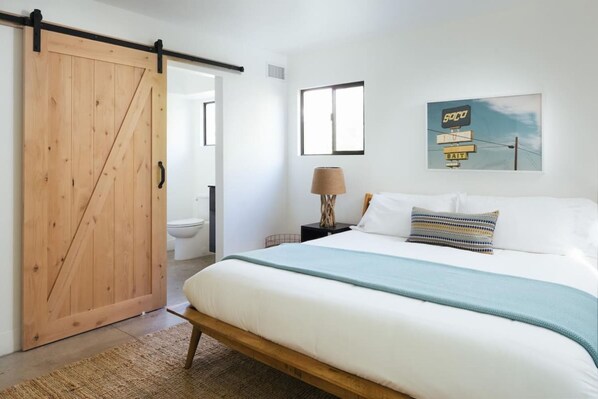 A bedroom with a wooden bed, a sliding door, a bedside lamp, and a wall-mounted artwork.
