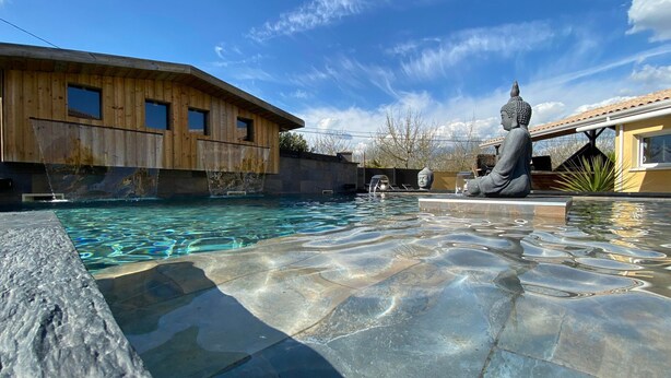 A swimming pool with clear water, a Buddha statue, and wooden buildings in the background. - Villa Naeva with swimming pool, Jacuzzi 10 places, Ping pong, plancha and Brasero (Agnac)
