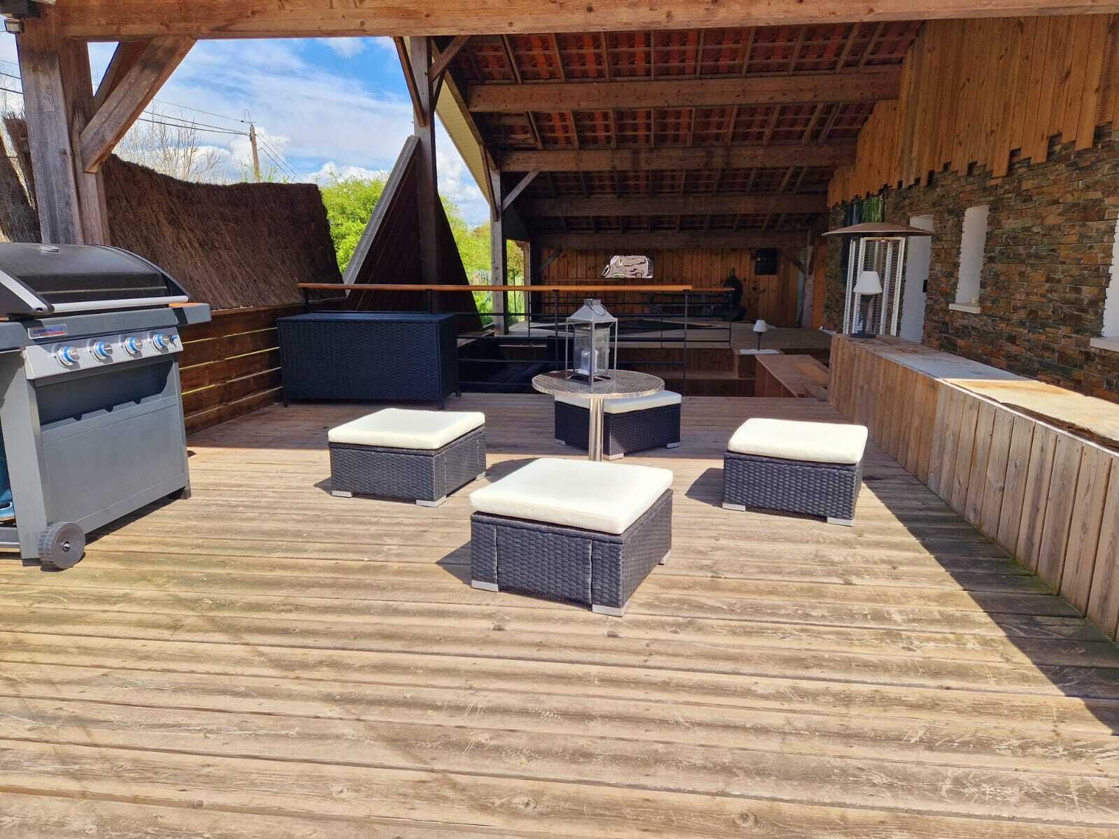 Un patio exterior con una parrilla, mobiliario de mimbre y un muro de piedra.