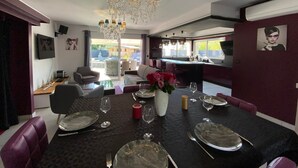 A dining area with a chandelier, dining table set for four, and a view of the outside. - Villa Naeva with swimming pool, Jacuzzi 10 places, Ping pong, plancha and Brasero (Agnac)