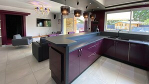 A modern kitchen with a central island, dark purple cabinets, and pendant lighting. - Villa Naeva with swimming pool, Jacuzzi 10 places, Ping pong, plancha and Brasero (Agnac)