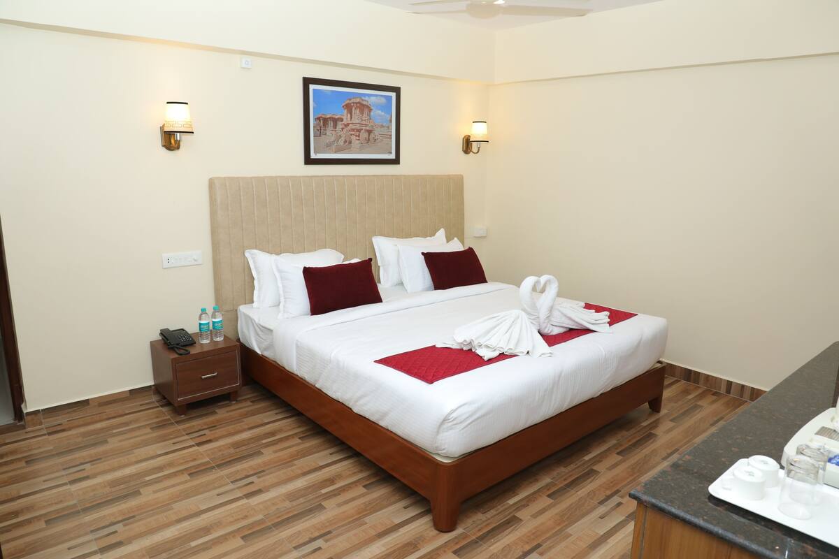 A hotel room with a large bed, wooden floor, two bedside tables, a nightstand, and a framed picture on the wall.