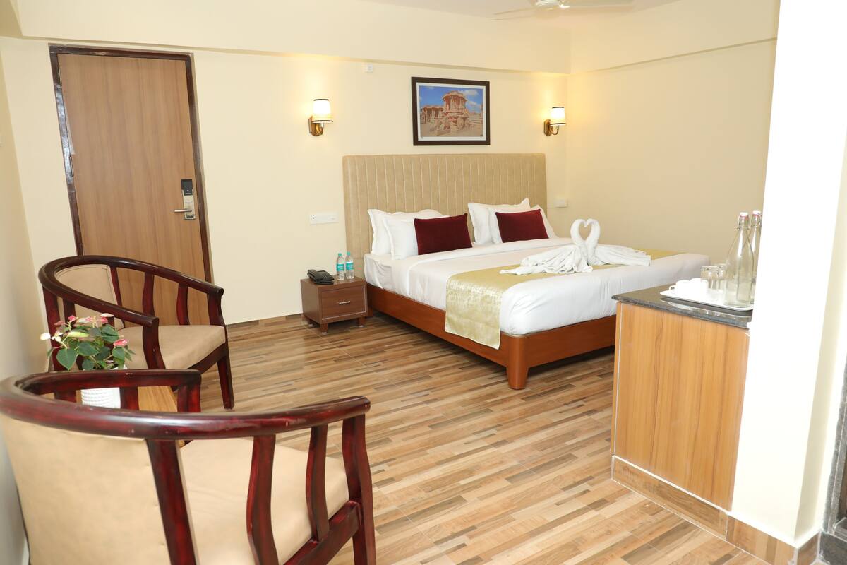 A hotel room with a wooden floor, a bed with white linens, a wooden chair, a nightstand with a phone, and a framed picture on the wall.