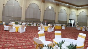 Un salón de banquetes con mesas redondas y sillas blancas, cada una con un lazo dorado.