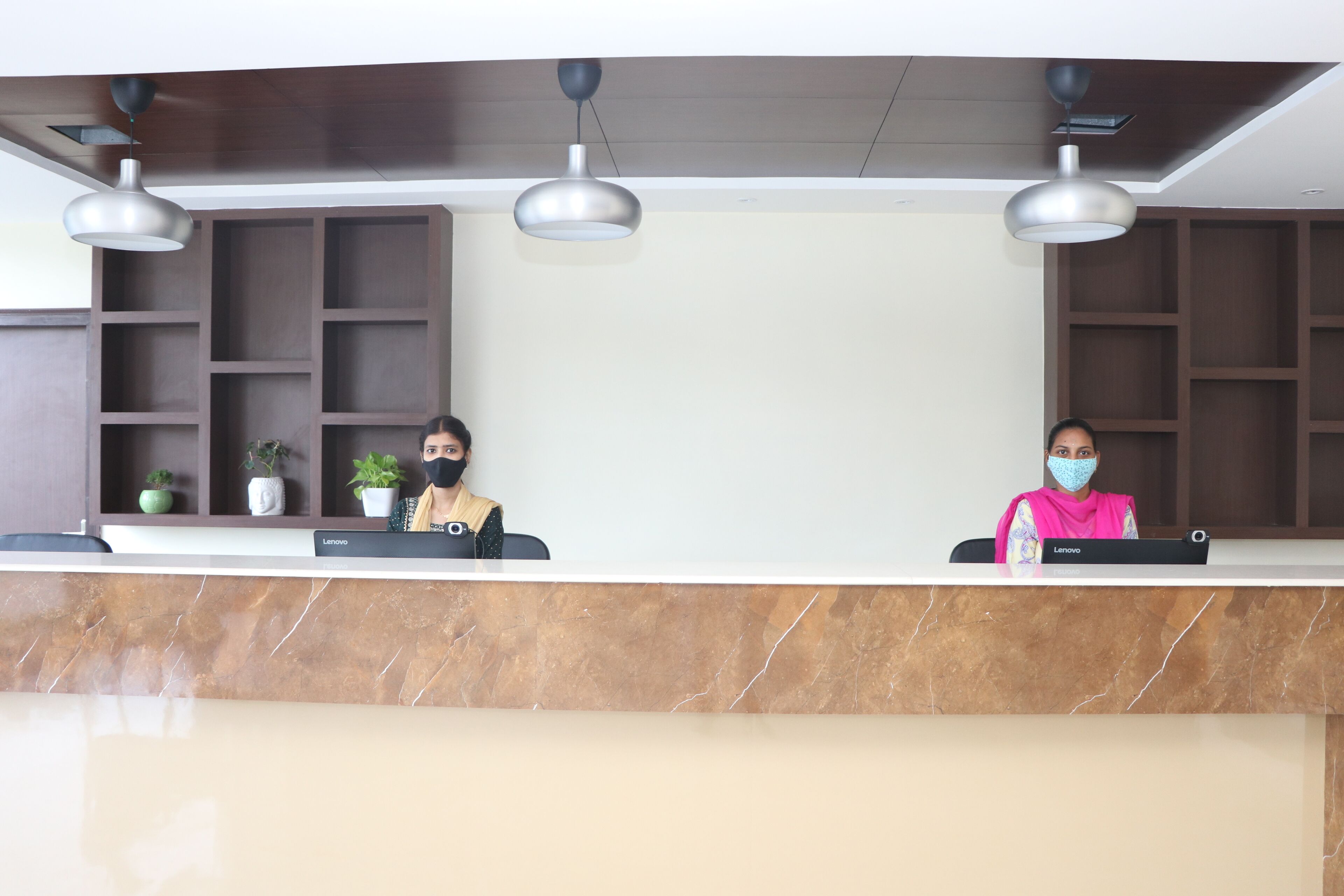 A reception desk with two staff members, a marble counter, and pendant lighting.