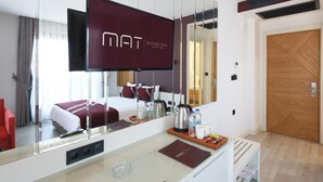 Habitación de hotel con un espejo grande, una cama con una manta roja, un televisor, una cafetera y una bandeja con aperitivos.