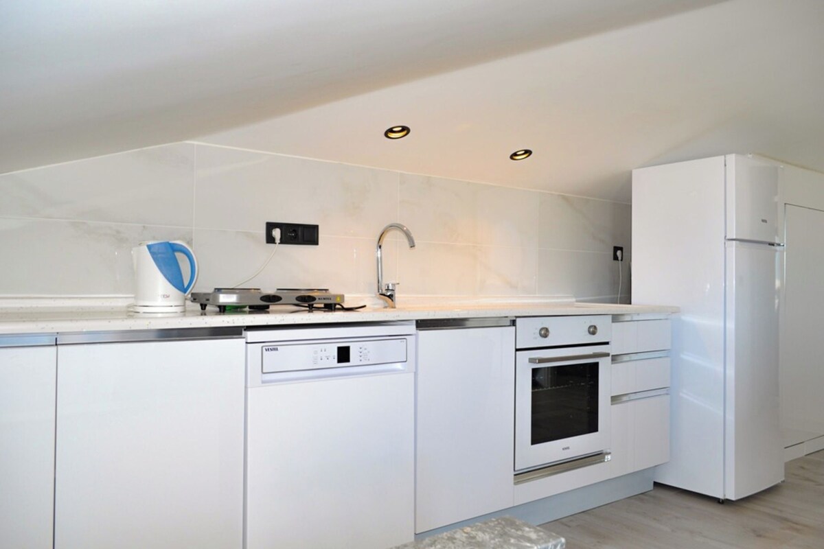 Une cuisine moderne avec des meubles blancs, un four encastré, un lave-vaisselle et un réfrigérateur.