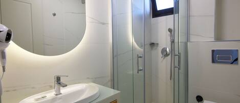 Un baño moderno con ducha envuelta en vidrio, un lavabo blanco y un espejo.