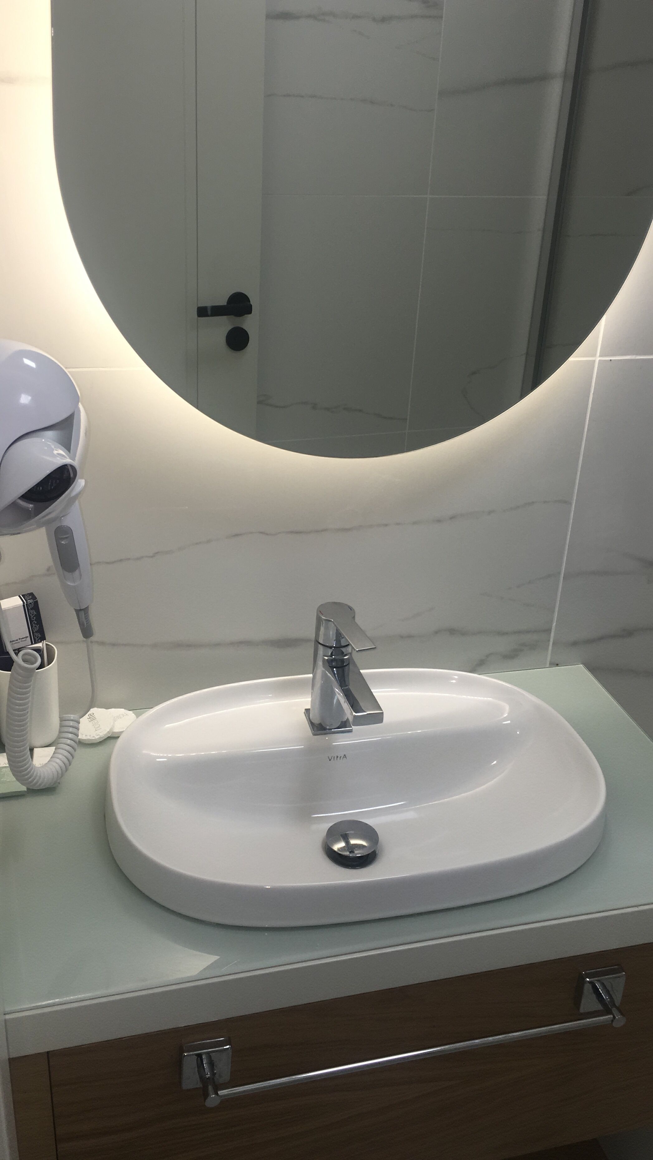 A bathroom with a white sink, a mirror with a circular frame, and a hairdryer on the counter.